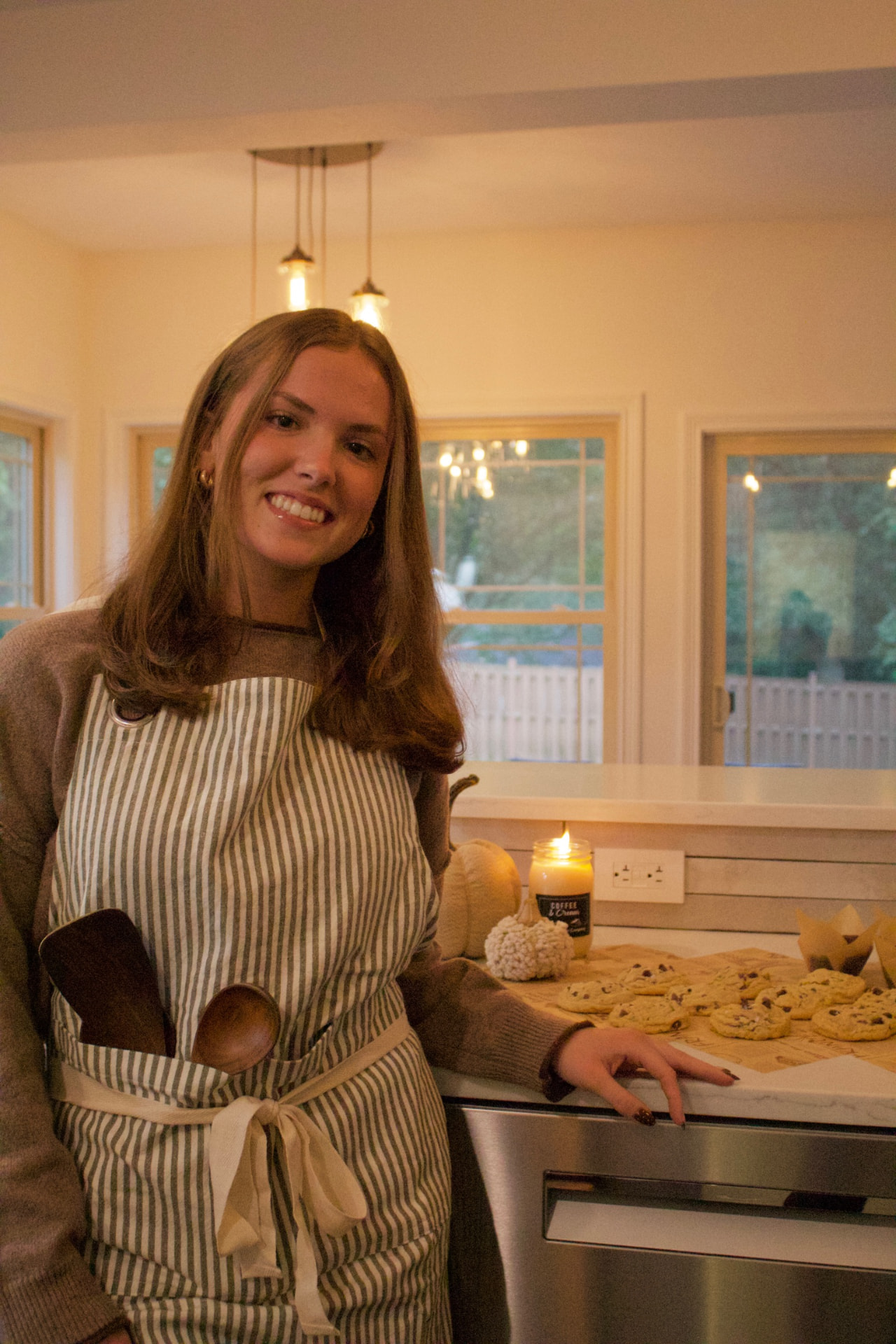 Alaena smiling in her kitchen, arranging fresh chocolate chip cookies and muffins on the counter